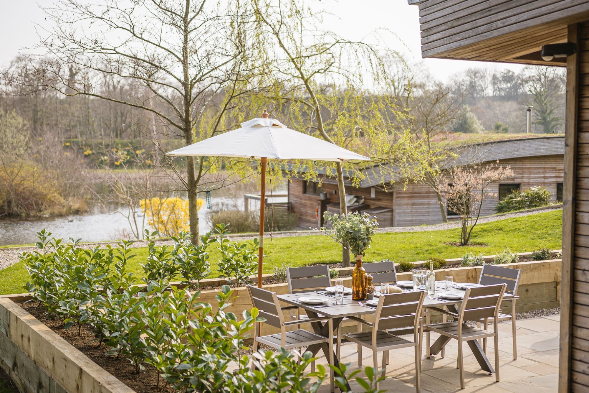 An outdoor patio with a table set for dining, surrounded by wooden chairs and a large umbrella.