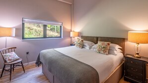 Une chambre à coucher avec un grand lit, deux lampes de chevet, une chaise, une table de chevet et une fenêtre donnant sur un paysage verdoyant.