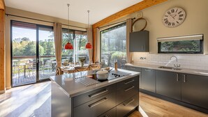 Une cuisine moderne dotée d’un grand îlot central, d’appareils électroménagers en acier inoxydable et offrant une vue sur l’extérieur.