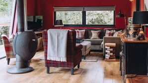 Ein gemütliches Wohnzimmer mit roter Wand, einer Couch, einem Sessel, einem Kamin und einem Bücherregal.
