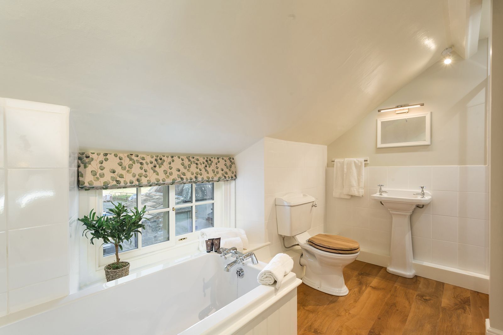 Ein Badezimmer mit Badewanne, Toilette, Waschbecken und einem Fenster mit Pflanze.