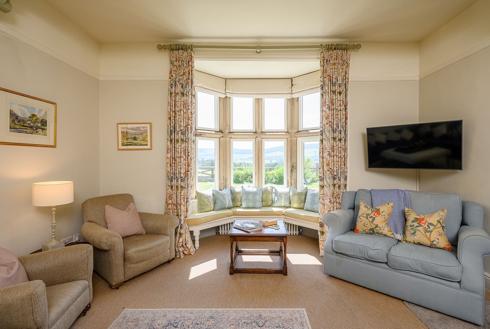 A cozy living room with a bay window, a sofa, a chair, a coffee table, and a television.