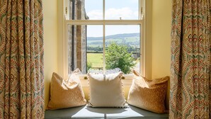 A window seat with cushions, a view of a green landscape, and patterned curtains. - Hollins Farmhouse -  a house that sleeps 10 guests  in 5 bedrooms (Leyburn)