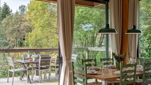 An outdoor dining area with a wooden deck, a table set for four, and a view of trees and greenery. - Cara -  a lodge that sleeps 6 guests  in 3 bedrooms (Richmond)