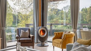 Una sala de estar moderna con chimenea de piedra, sofás de cuero y vista a un lago y árboles.
