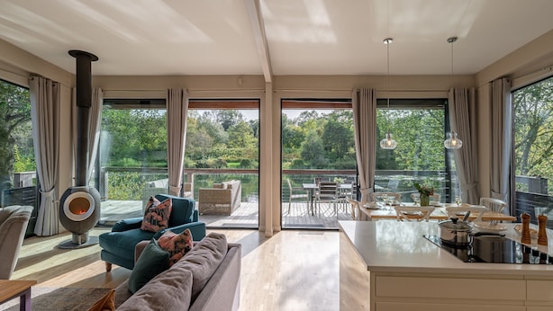 A spacious living area with a large sofa, a dining table set for two, and a view of a lake through large windows. - Finley -  a lodge that sleeps 6 guests  in 3 bedrooms (Richmond)