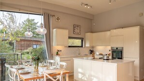 A modern kitchen with white cabinetry, a central island, and a dining area with a wooden table and white chairs. - Finley -  a lodge that sleeps 6 guests  in 3 bedrooms (Richmond)