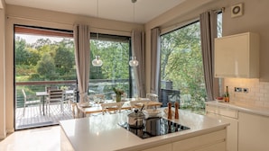 A modern kitchen with a large island, a dining area with a view of a pond, and a balcony with a table and chairs. - Finley -  a lodge that sleeps 6 guests  in 3 bedrooms (Richmond)