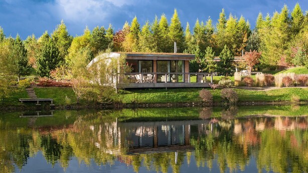 Järvenrantahuvila, jossa on terassi, jolta avautuu näkymä lammelle. Huvilaa ympäröi tiheä metsä.