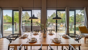 Un coin repas avec une grande table dressée pour six personnes, de grandes fenêtres et une vue sur un lac.
