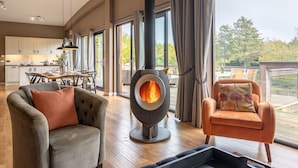 Un vaste espace de vie doté d’une cheminée moderne, d’un coin repas et d’un balcon offrant une vue sur les arbres.