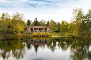 A lakeside cabin with a deck and large windows, surrounded by trees and a calm lake.