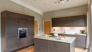 A modern kitchen with dark wood cabinets, a central island, a built-in oven, and a stainless steel sink. - Juniper -  a lodge that sleeps 6 guests  in 3 bedrooms (Richmond)