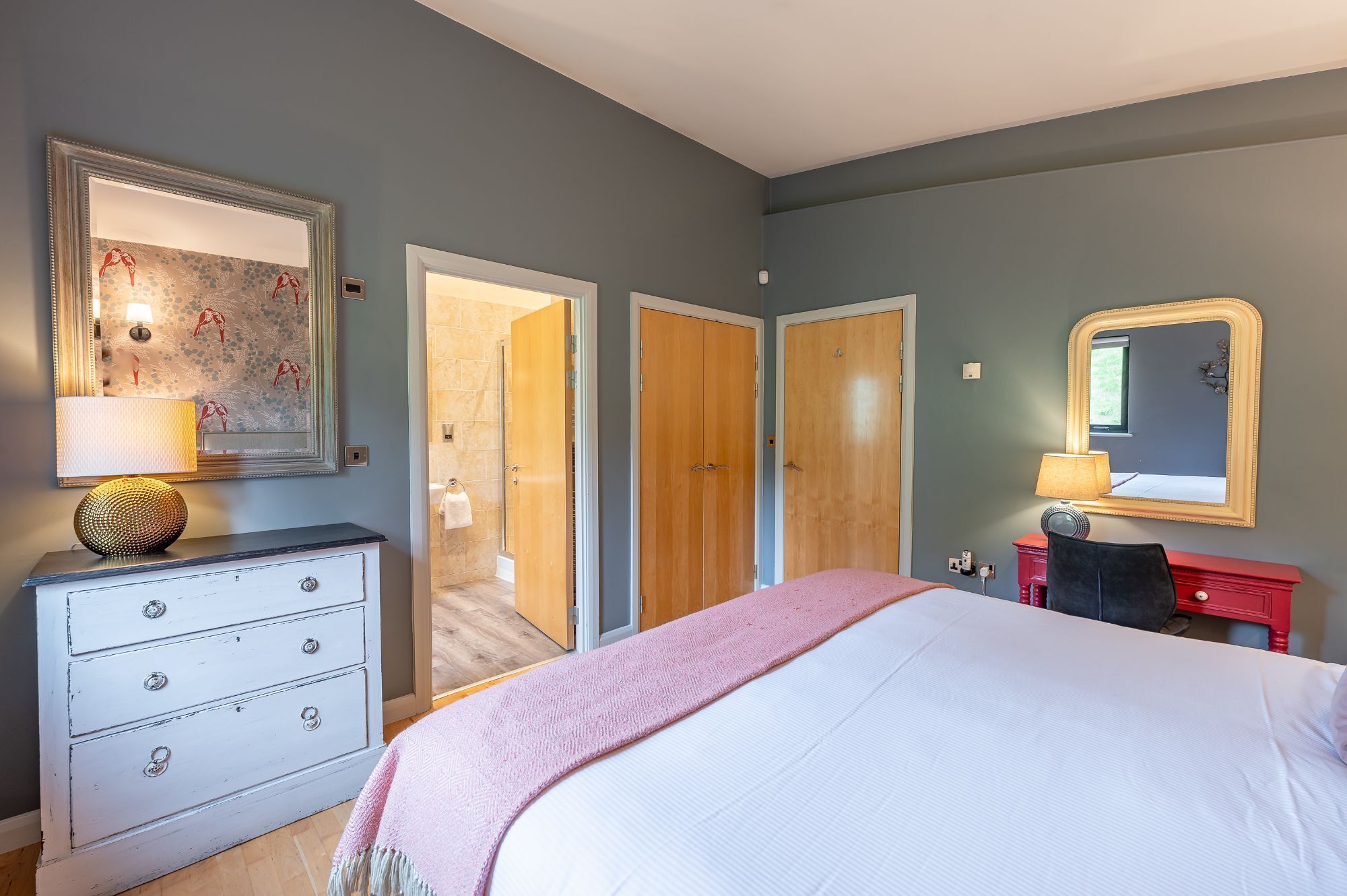 Een slaapkamer met een bed, een dressoir, een spiegel en een kledingkast.