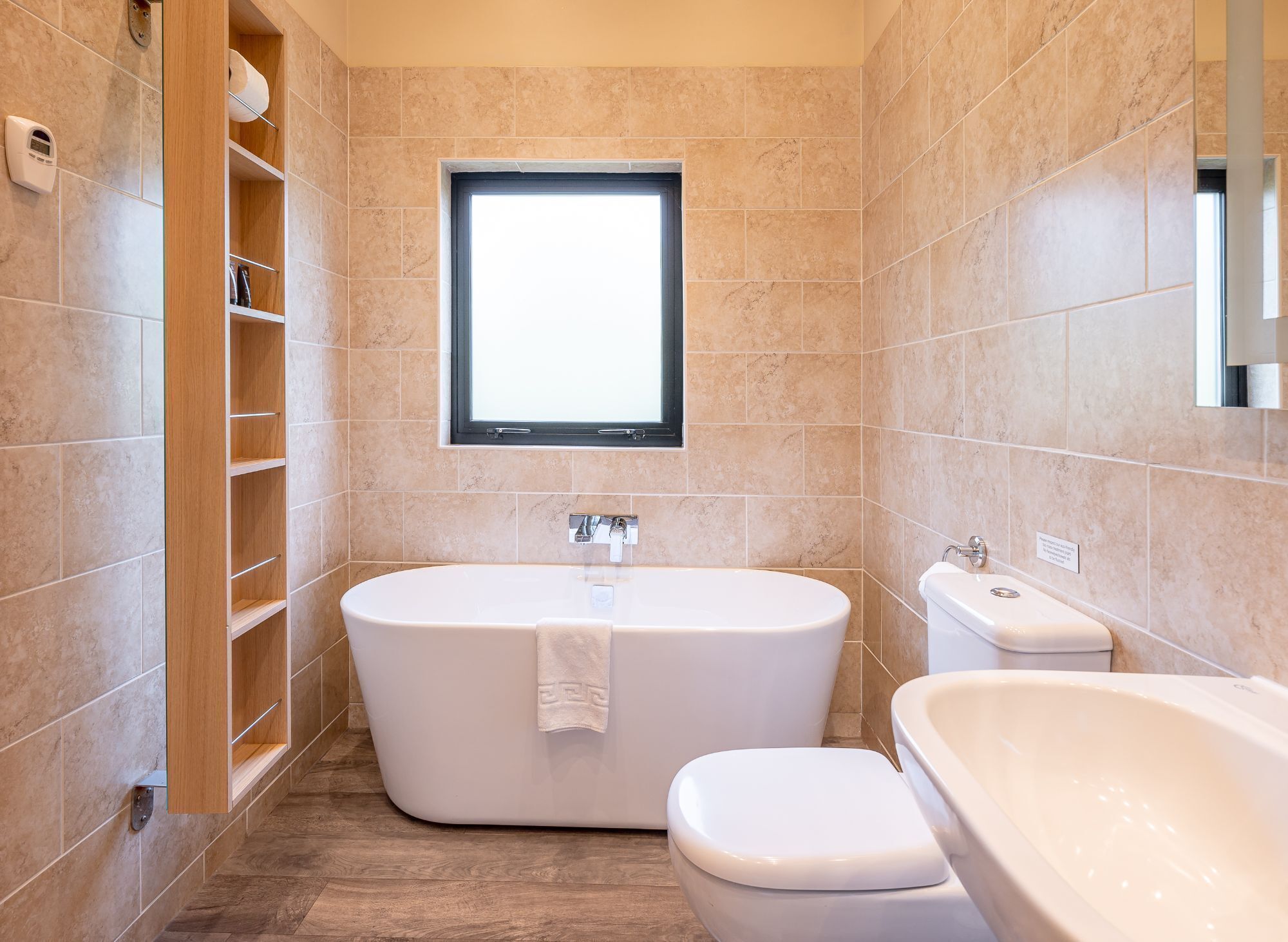 Een moderne badkamer met een vrijstaand bad, een toilet en een raam voor natuurlijk licht.