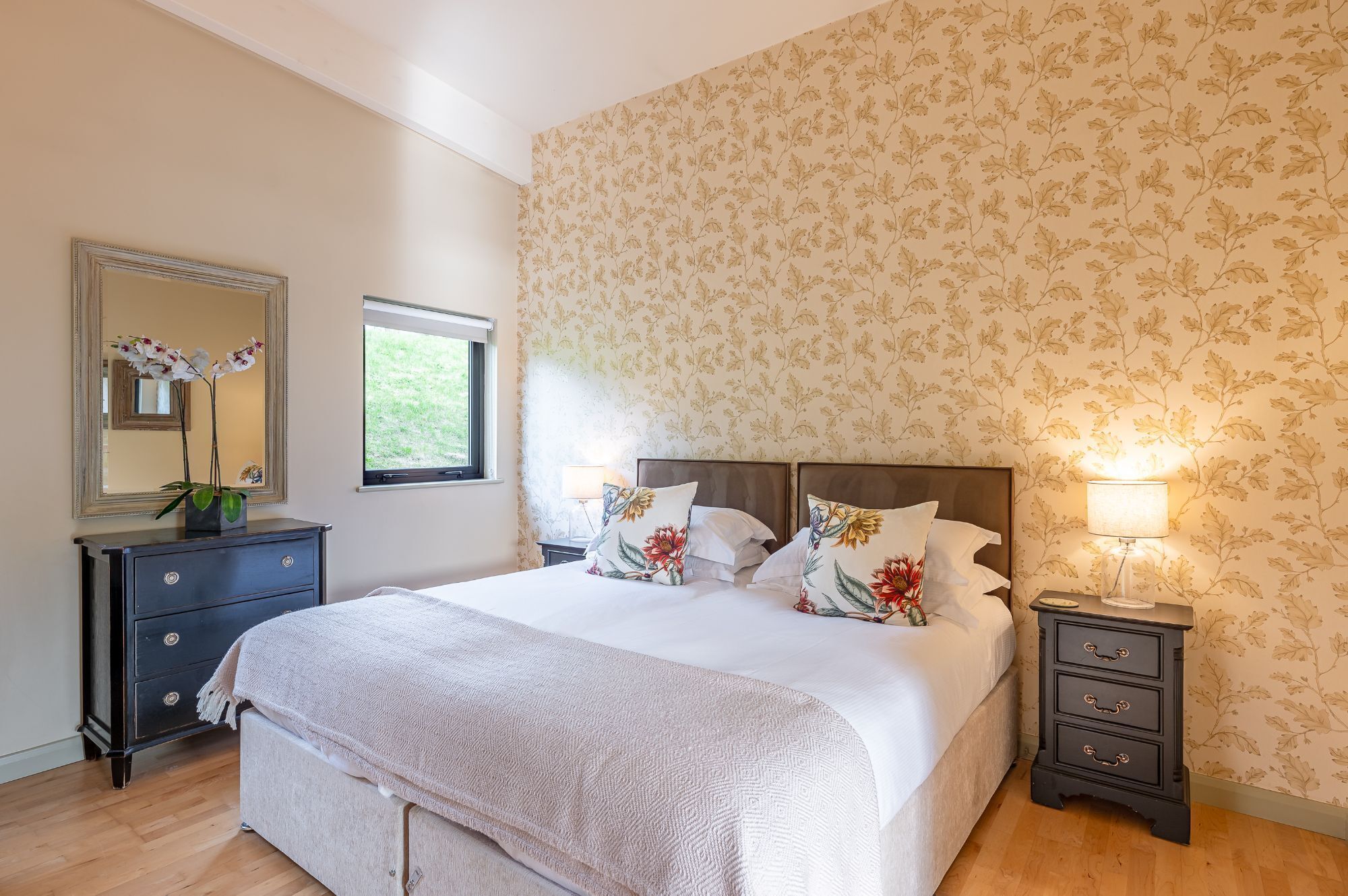 Een slaapkamer met een bed, een kaptafel, een nachtkastje, een lamp, een raam en een spiegel.