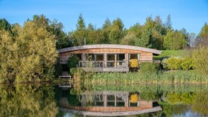 A modern house with a curved roof, a deck, and a reflection in the water. - Juniper -  a lodge that sleeps 6 guests  in 3 bedrooms (Richmond)