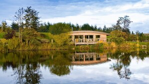A lakeside wooden cabin with a deck, surrounded by lush greenery and trees. - Louis -  a lodge that sleeps 6 guests  in 3 bedrooms (Richmond)