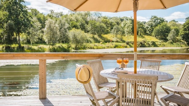 A wooden deck with a table and chairs, overlooking a calm body of water and lush greenery. - Louis -  a lodge that sleeps 6 guests  in 3 bedrooms (Richmond)
