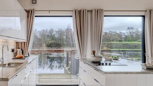 A modern kitchen with a large window, a view of a lake, and a dining area with a table and chairs. - Lulu -  a lodge that sleeps 6 guests  in 3 bedrooms (Near Richmond)