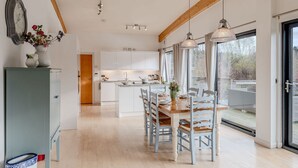 A modern kitchen with white cabinets, a dining area with a wooden table and chairs, and large windows offering a view of the outdoors. - Lulu -  a lodge that sleeps 6 guests  in 3 bedrooms (Near Richmond)