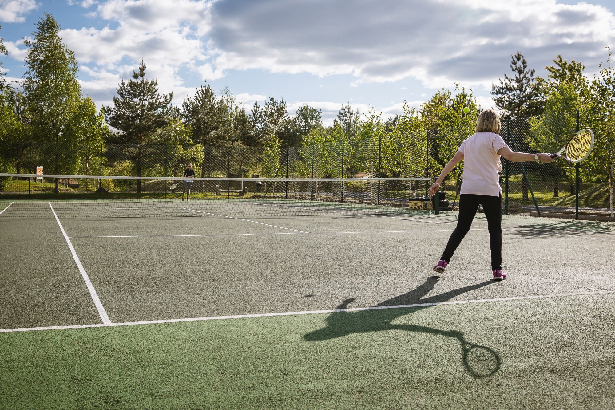 A tennis court with a net, surrounded by trees and a clear sky.