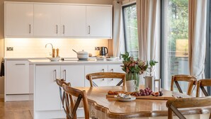 A modern kitchen with white cabinets, a wooden dining table, and a large window with curtains. - Charlie -  a lodge that sleeps 6 guests  in 3 bedrooms (Richmond)