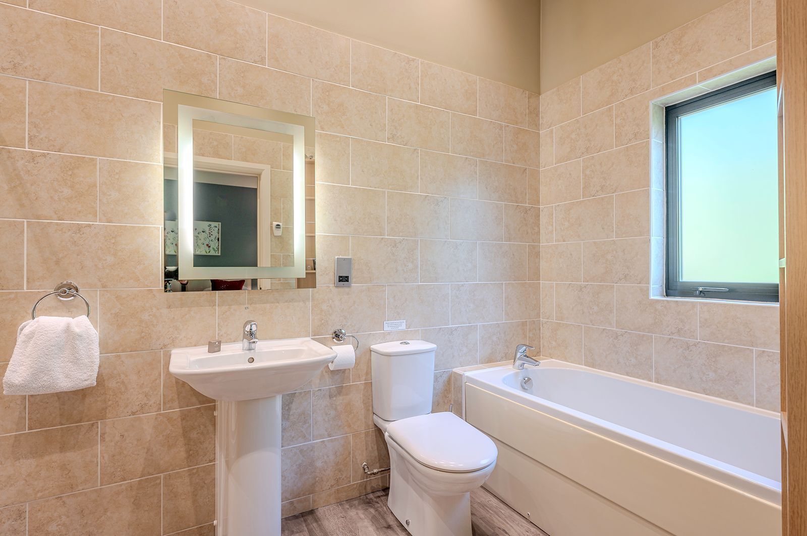 A bathroom with beige tiles, a sink, toilet, and bathtub.