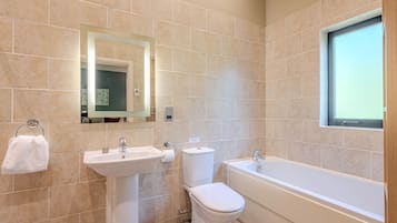 A bathroom with beige tiles, a sink, toilet, and bathtub.