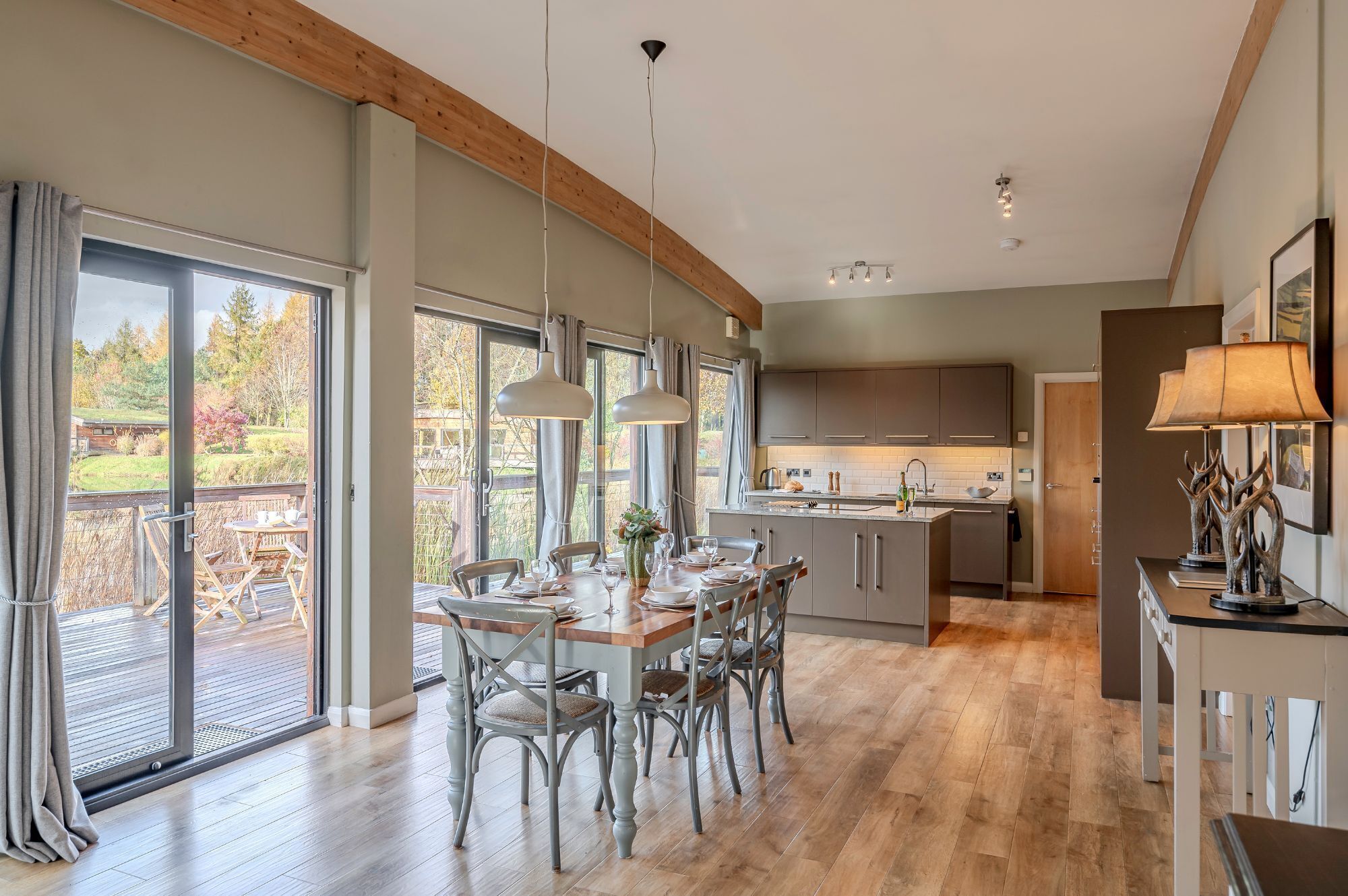 Een moderne keuken met een centraal eiland, grote ramen en een eetgedeelte met houten stoelen en een tafel.