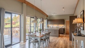 Et moderne køkken med en central ø, store vinduer og et spiseområde med træstole og et bord.