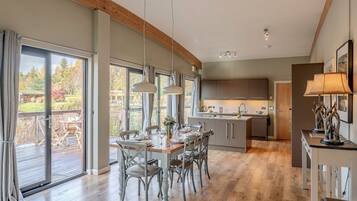 Een moderne keuken met een centraal eiland, grote ramen en een eetgedeelte met houten stoelen en een tafel.