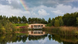 A lakeside building with a reflection in the water, surrounded by trees and vegetation.