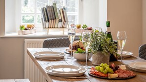 Una mesa de comedor dispuesta con platos, copas, una botella de champán y una variedad de quesos y embutidos.