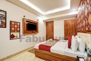 Une chambre à coucher avec un lit en bois, un téléviseur fixé au mur et une armoire dont les portes sont recouvertes d’un papier peint à motifs.