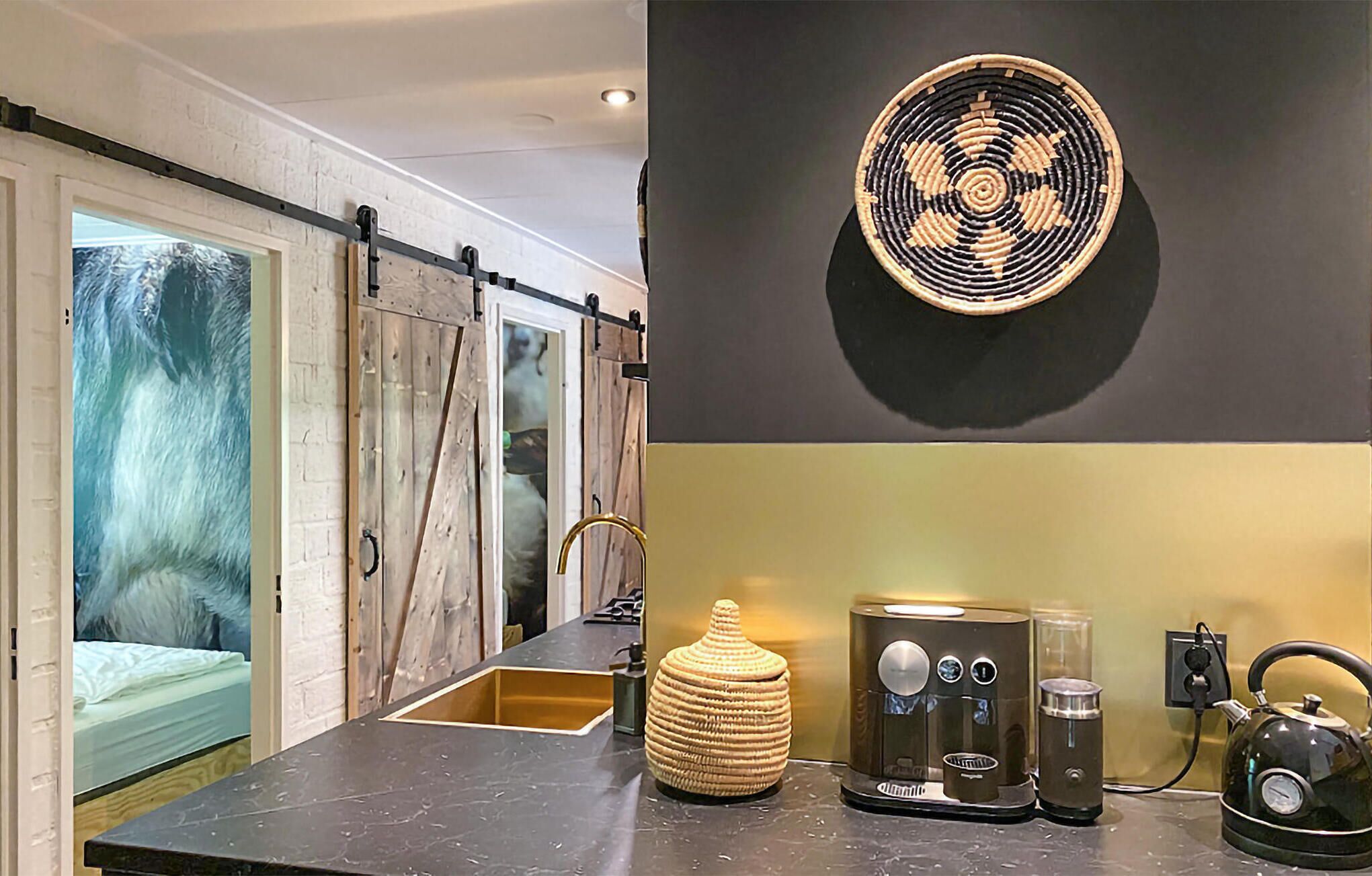 A kitchen with a black countertop, a coffee machine, a kettle, and a woven basket on the wall.