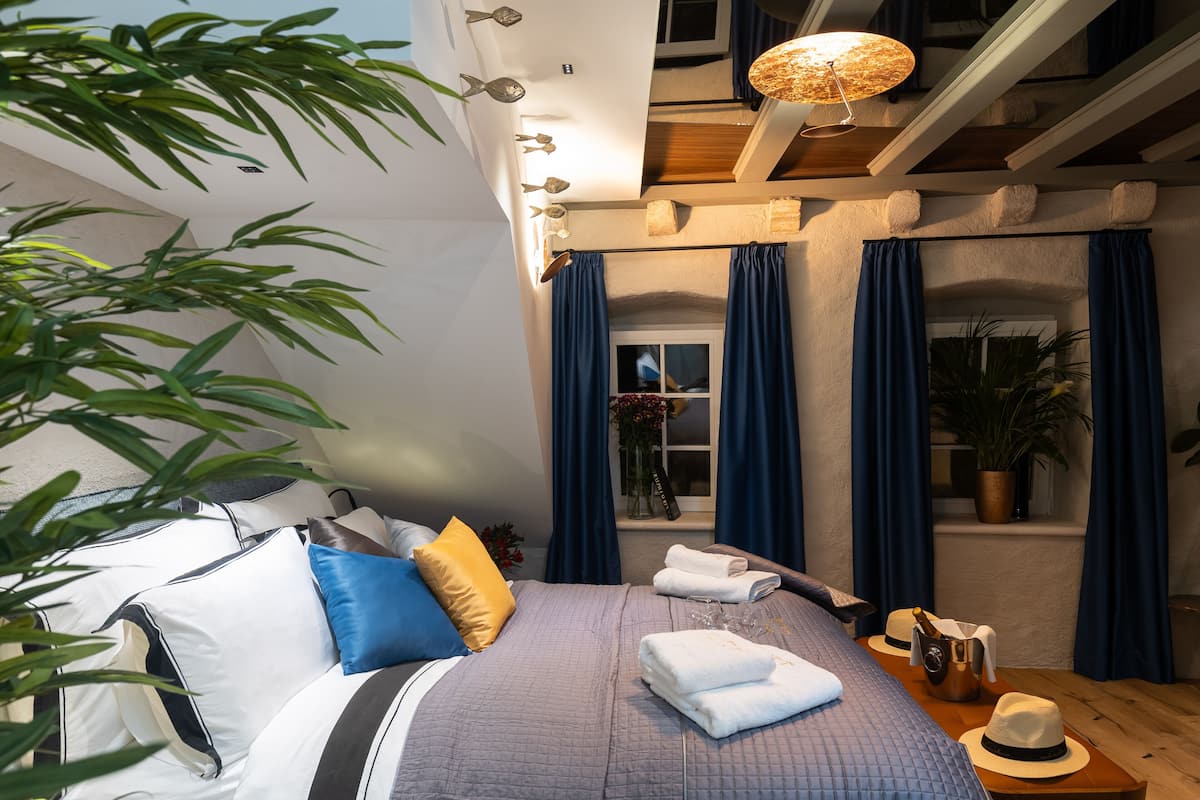 Un dormitorio bien iluminado con cama, almohadas, una mesita de noche con un sombrero y una planta en maceta.