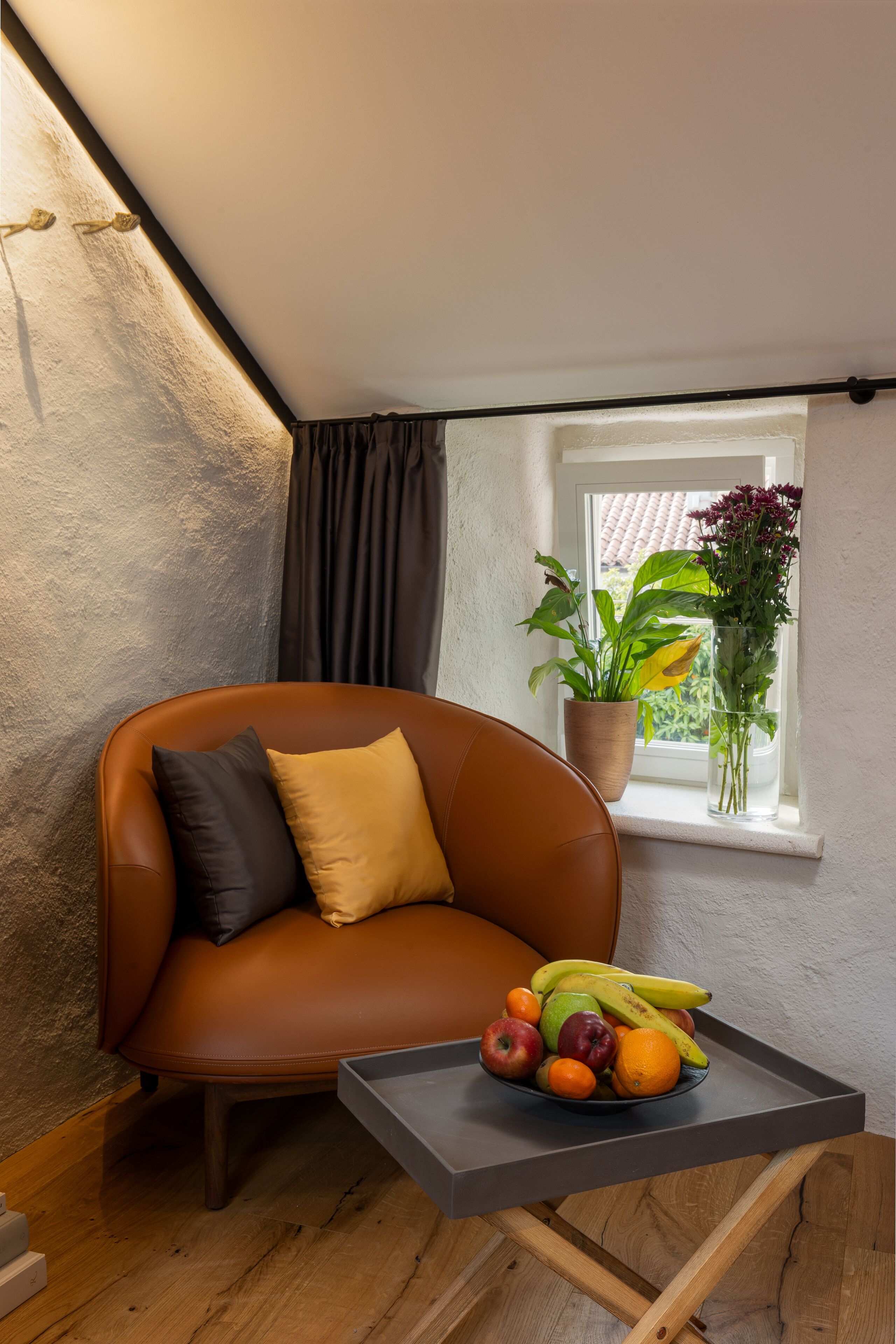 A cozy corner with a brown leather chair, a small table with fruits and a potted plant by a window.