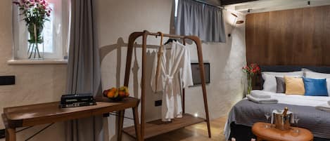 A bedroom with a wooden bed, a bedside table with a book and a bottle, a wooden chair, and a window with curtains.