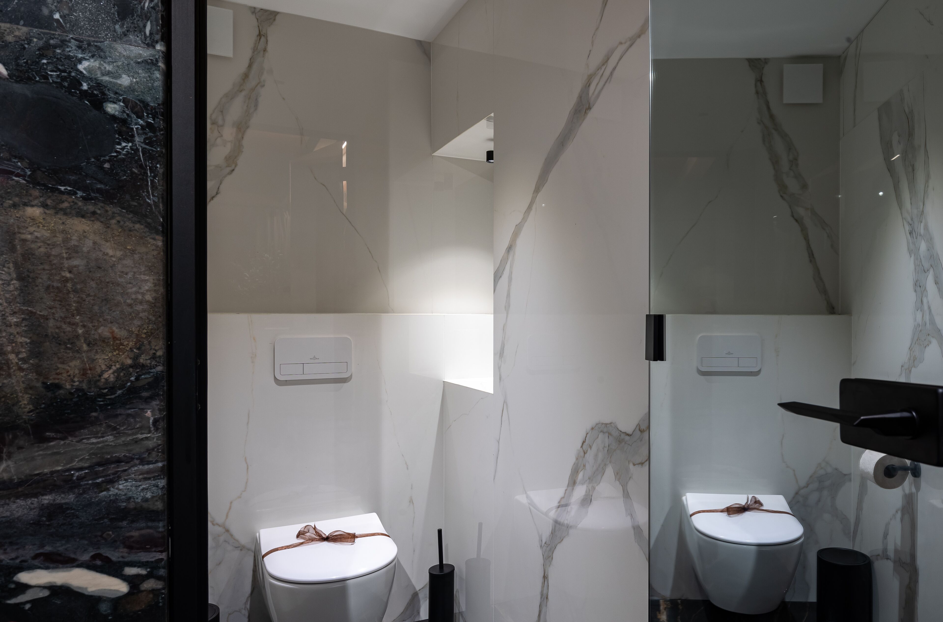 A modern bathroom with two toilets, marble walls, and a black sink.
