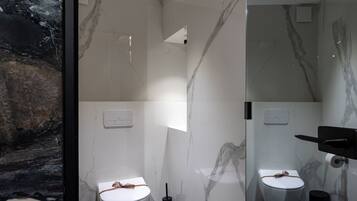 Un baño moderno con dos inodoros, paredes de mármol y un lavamanos negro.