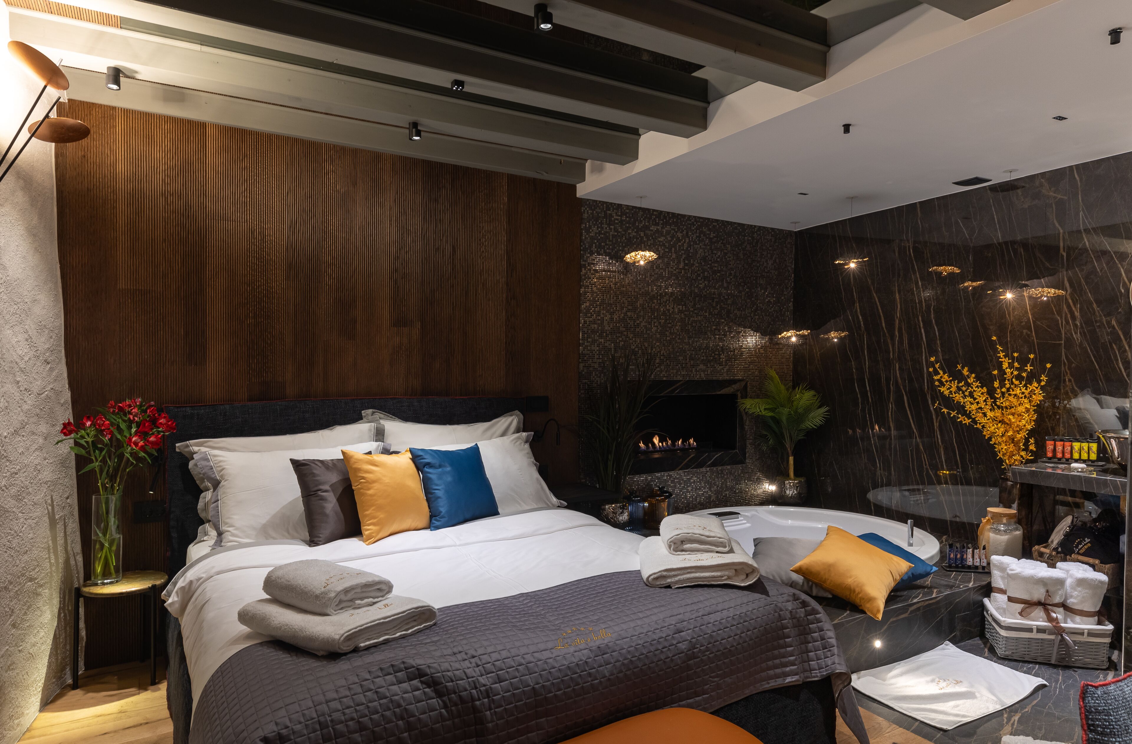 A modern hotel room with a large bed, a fireplace, a small table with toiletries, and a view of the city.