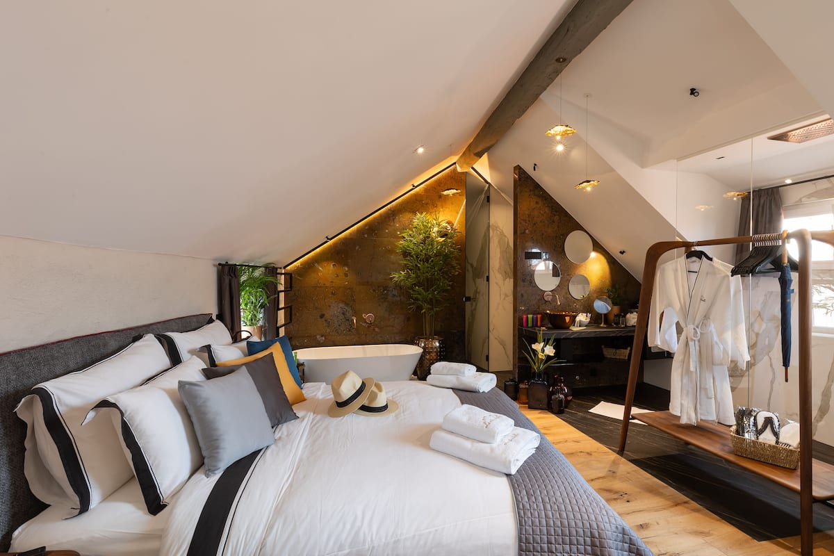Una habitación de hotel moderna con una cama grande, techo de madera y un baño visible al fondo.