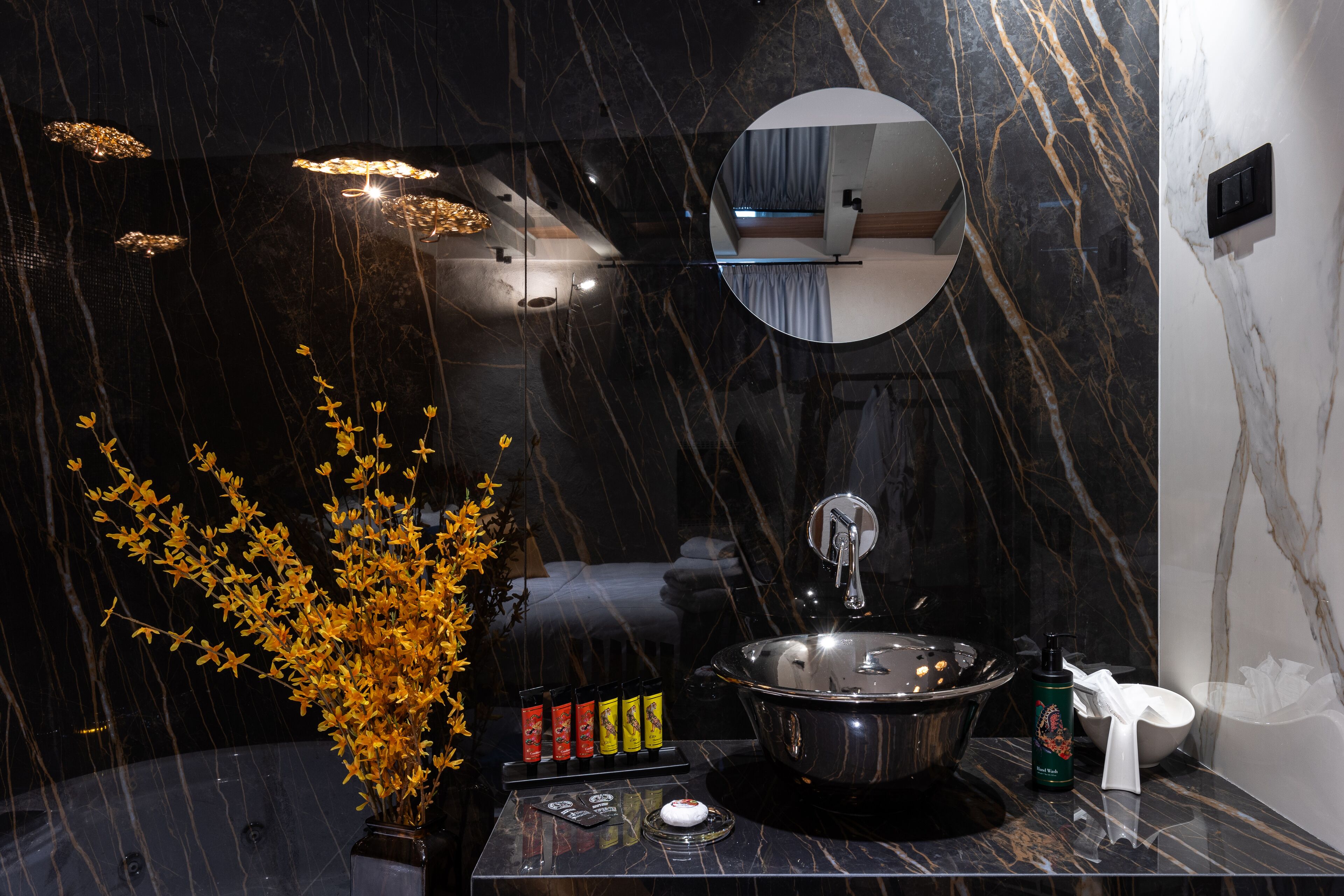 A modern bathroom with a black marble sink, a mirror, and a vase with yellow flowers.