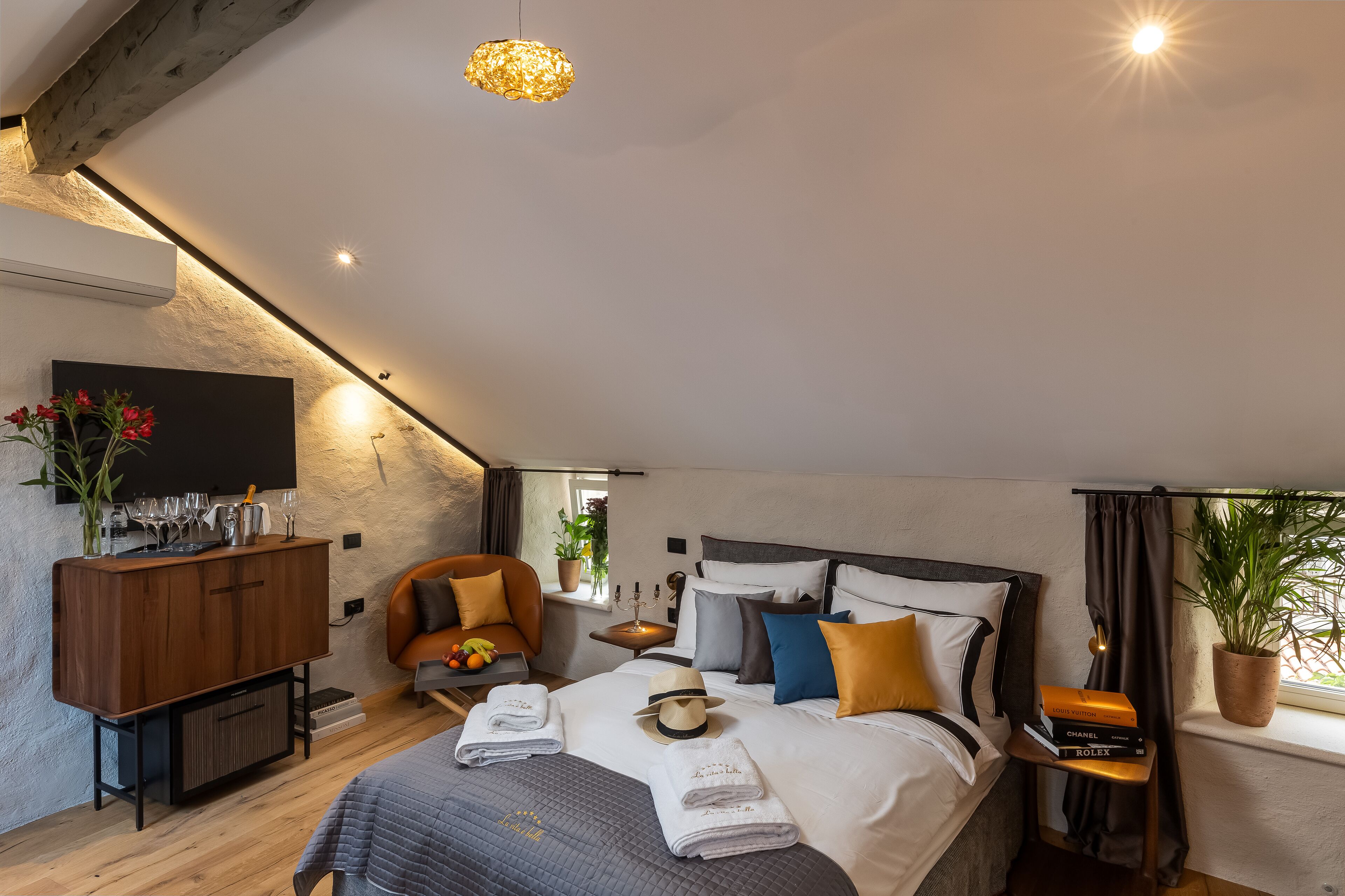 A modern bedroom with a large bed, bedside tables, a TV, and a potted plant by the window.