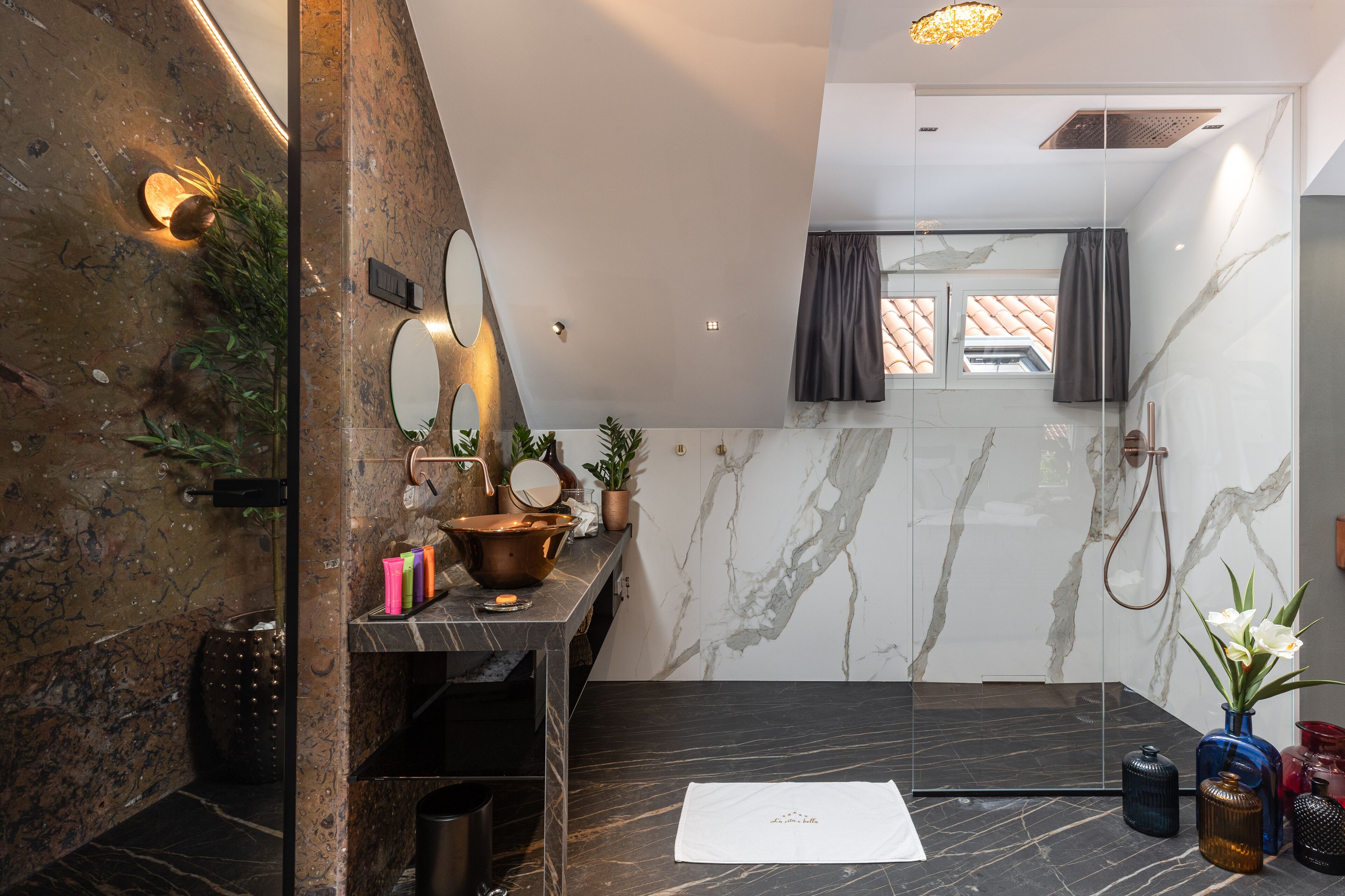 A modern bathroom with a marble vanity, a shower, and a small window.