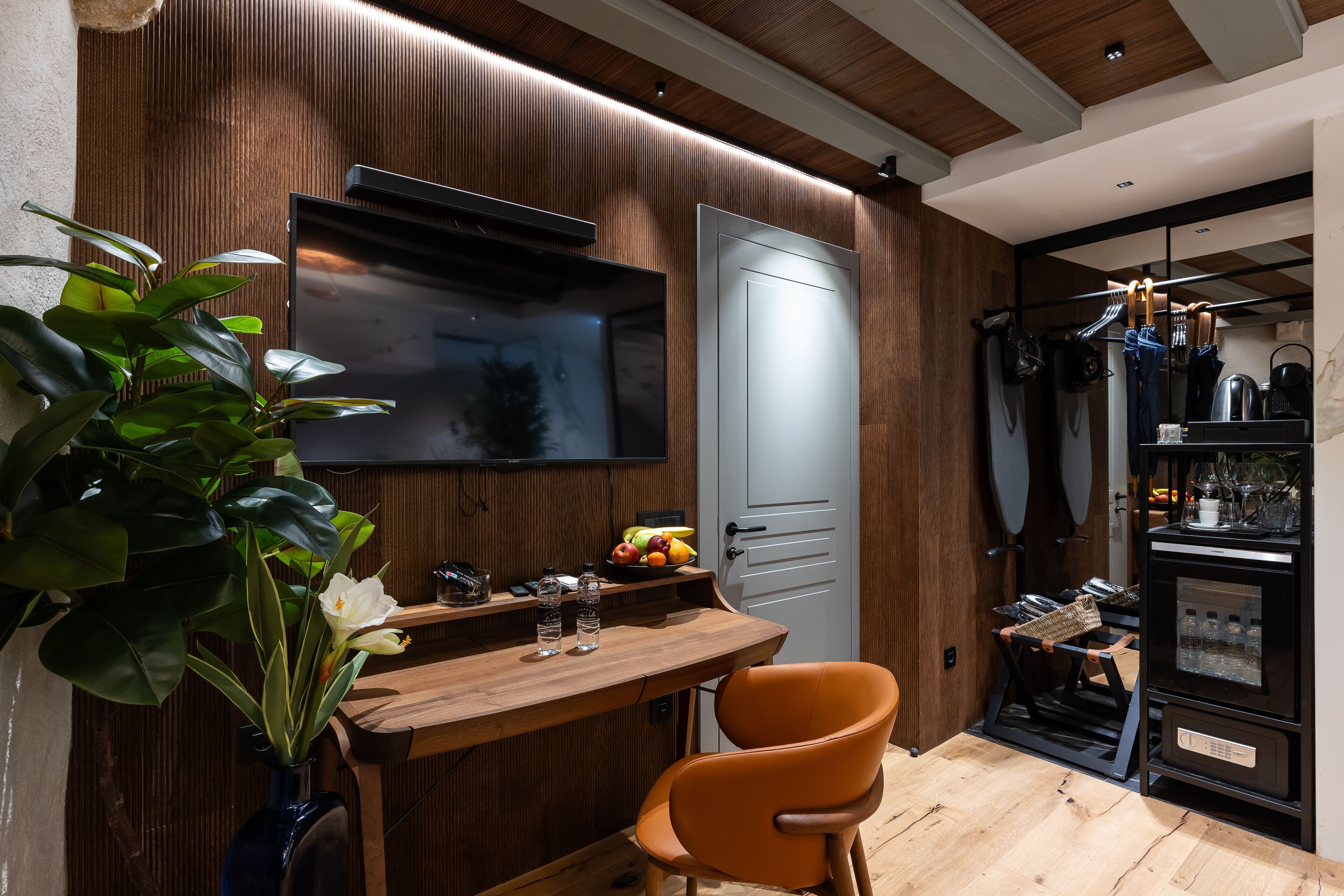 A modern kitchen with a wooden wall, a built-in TV, a fruit bowl, and a coffee machine.