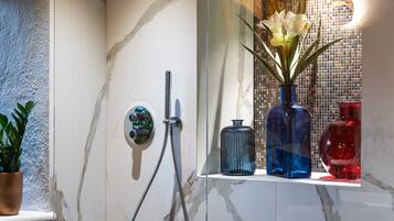 Un baño moderno con cabina de ducha de vidrio, paredes de mármol y un estante con jarrones decorativos.