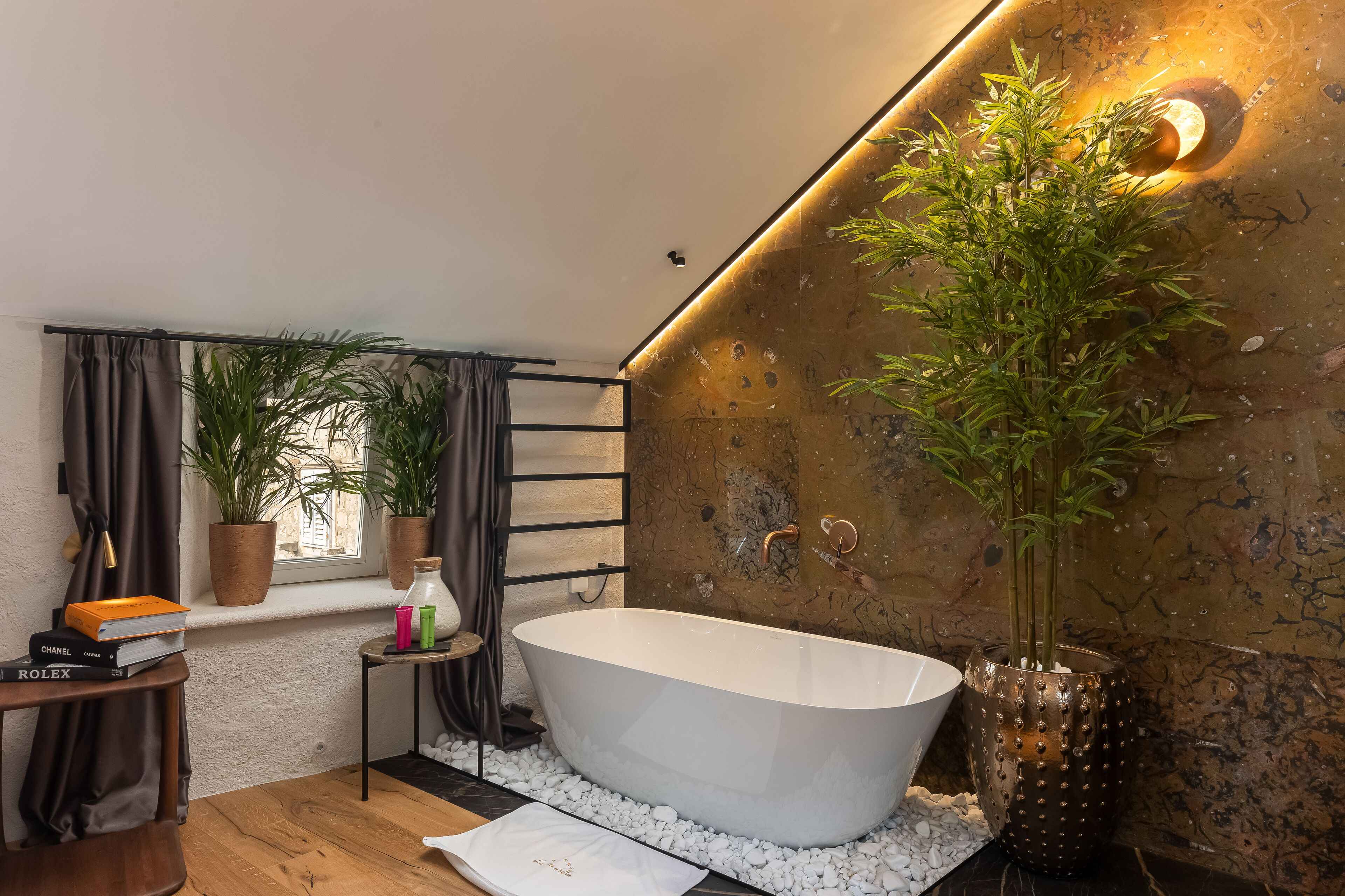 A modern bathroom with a freestanding bathtub, potted plants, and a window with curtains.