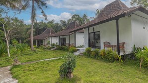A row of white buildings with tiled roofs, surrounded by lush greenery and palm trees. - Radjes Bungalow Nusa Penida (Penida Island)